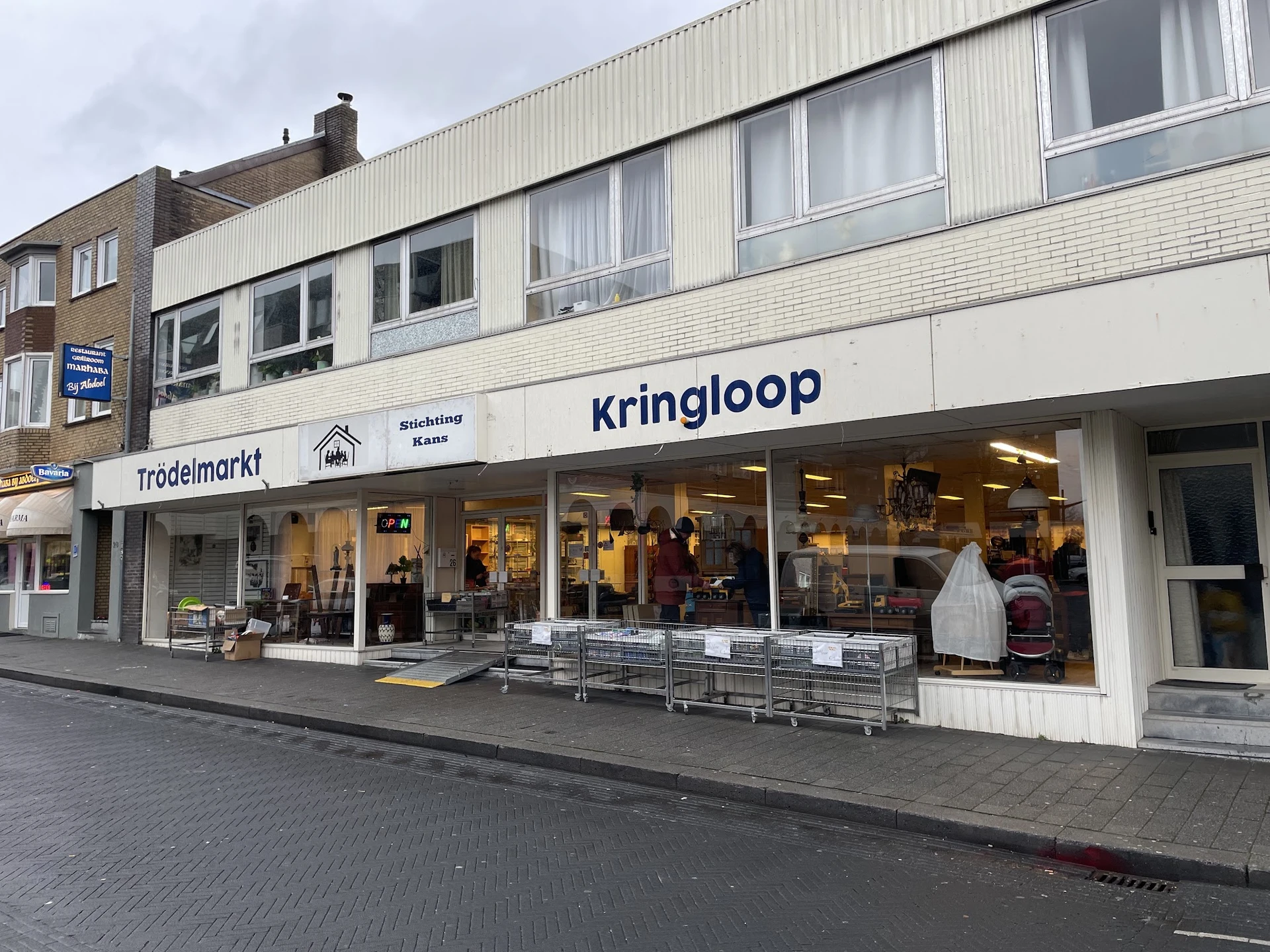 Voorgevel van kringloopwinkel met winkelnaam Kringloop zichtbaar, etalageruiten met tweedehands spullen, ingang met deur, str
