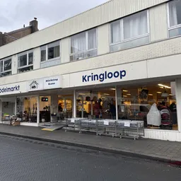 Voorgevel van kringloopwinkel met winkelnaam Kringloop zichtbaar, etalageruiten met tweedehands spullen, ingang met deur, str