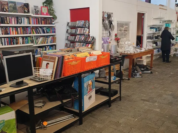 Winkelvloer met stellingen, boekenkasten, werkbanken en diverse tweedehands spullen, een persoon in het achtergrond