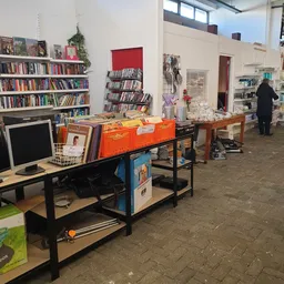 Winkelvloer met stellingen, boekenkasten, werkbanken en diverse tweedehands spullen, een persoon in het achtergrond