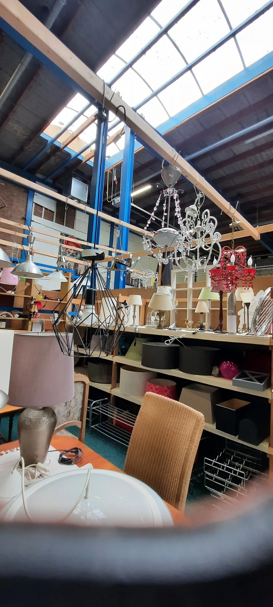 Diverse lampen en kroonluchters in verschillende stijlen op een tafel en aan het plafond in een kringloopwinkel