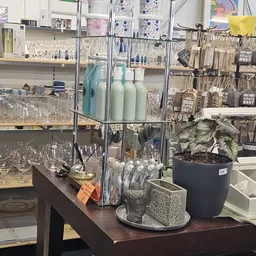 Glazen kasten met huishoudelijke artikelen, glazen, flessen en een potplant met decoratieve items op een werktafel