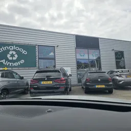 Voorgevel van Kringloop Almere met groen uithangbord en grijze metalen gevel, parkeerplaats met auto's ervoor