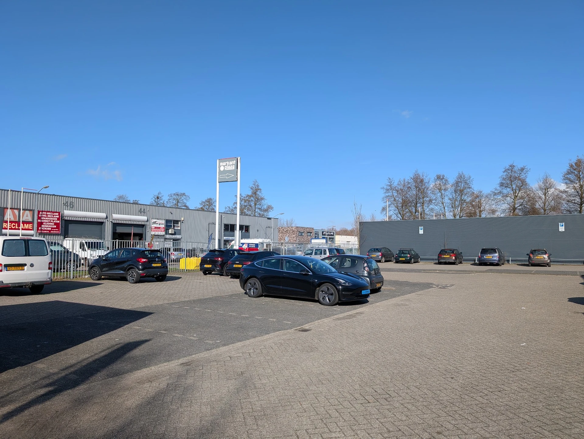 Parkeerterrein met geparkeerde auto's voor een grijze bedrijfsgebouw met wit bord