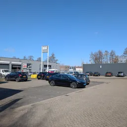 Parkeerterrein met geparkeerde auto's voor een grijze bedrijfsgebouw met wit bord