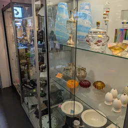 Vitrinekasten met uitgestalde glazen flessen, parfumflessen, decoratieve bollen en serviesgoed
