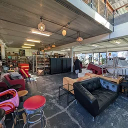 Ruime winkelvloer met rode en zwarte fauteuils, tafels en diverse meubels uitgestald onder betonnen plafond met hangende lamp
