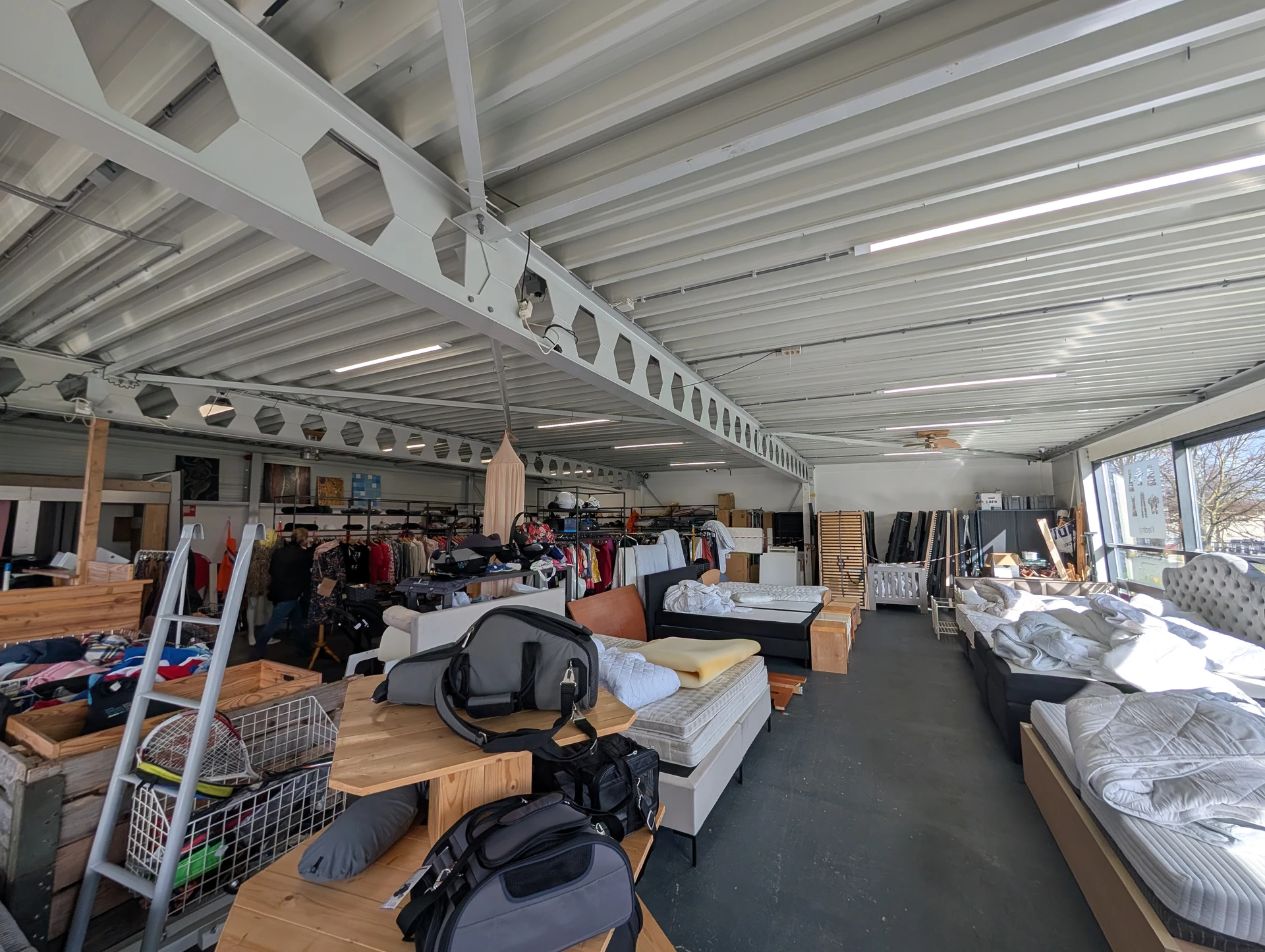 Ruim magazijn met stellingen vol tweedehands spullen, meubels en kleding onder industrieel plafond