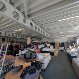 Ruim magazijn met stellingen vol tweedehands spullen, meubels en kleding onder industrieel plafond