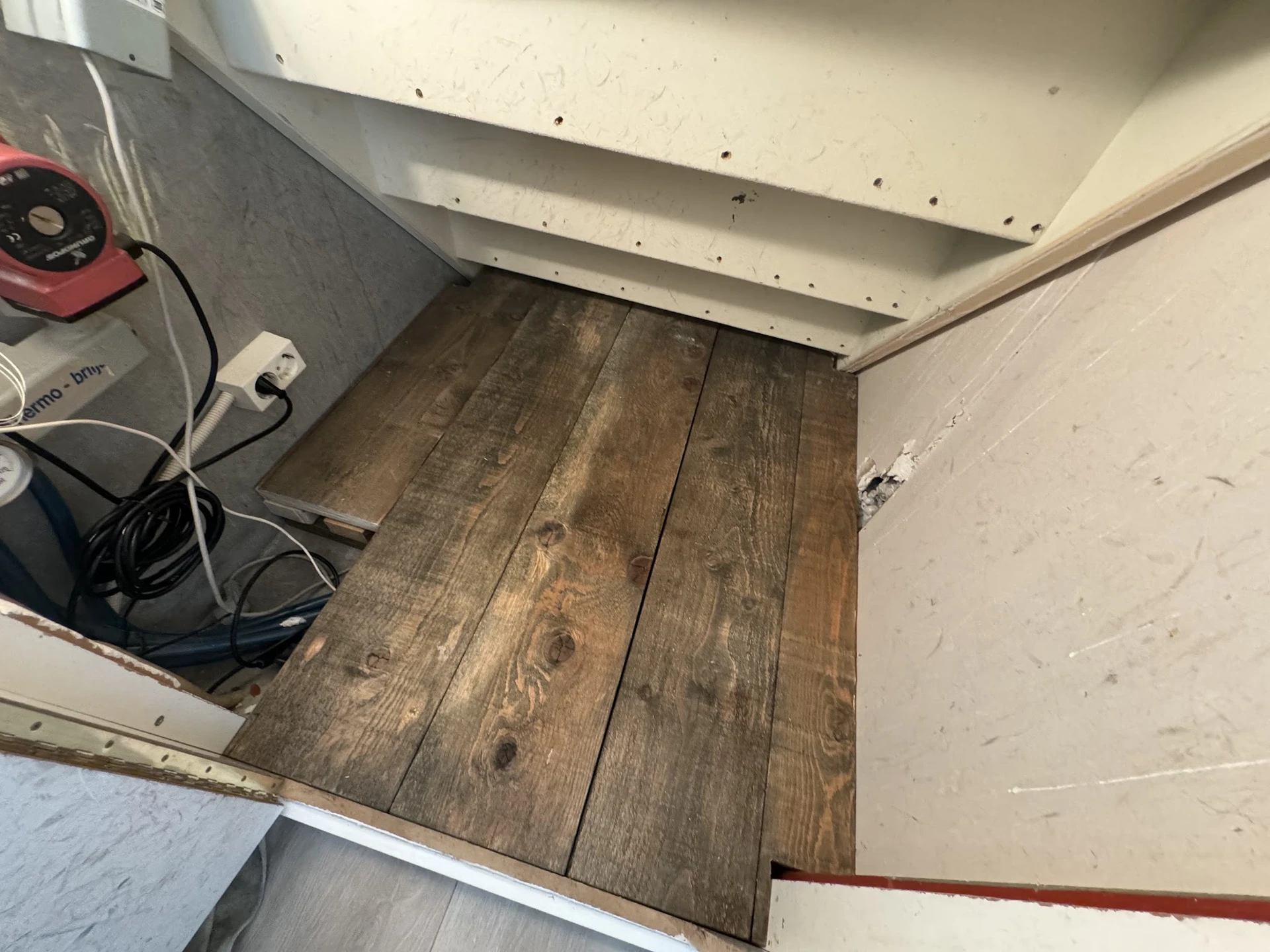 Winkelvloer met houten planken en witte muren, enkele apparaten in hoek