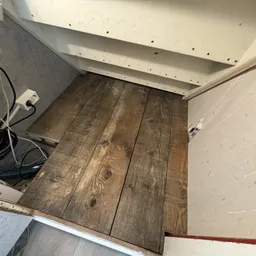 Winkelvloer met houten planken en witte muren, enkele apparaten in hoek