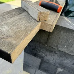 Close-up van een houten werkstuk op een steenachtergrond met gereedschap op de achtergrond
