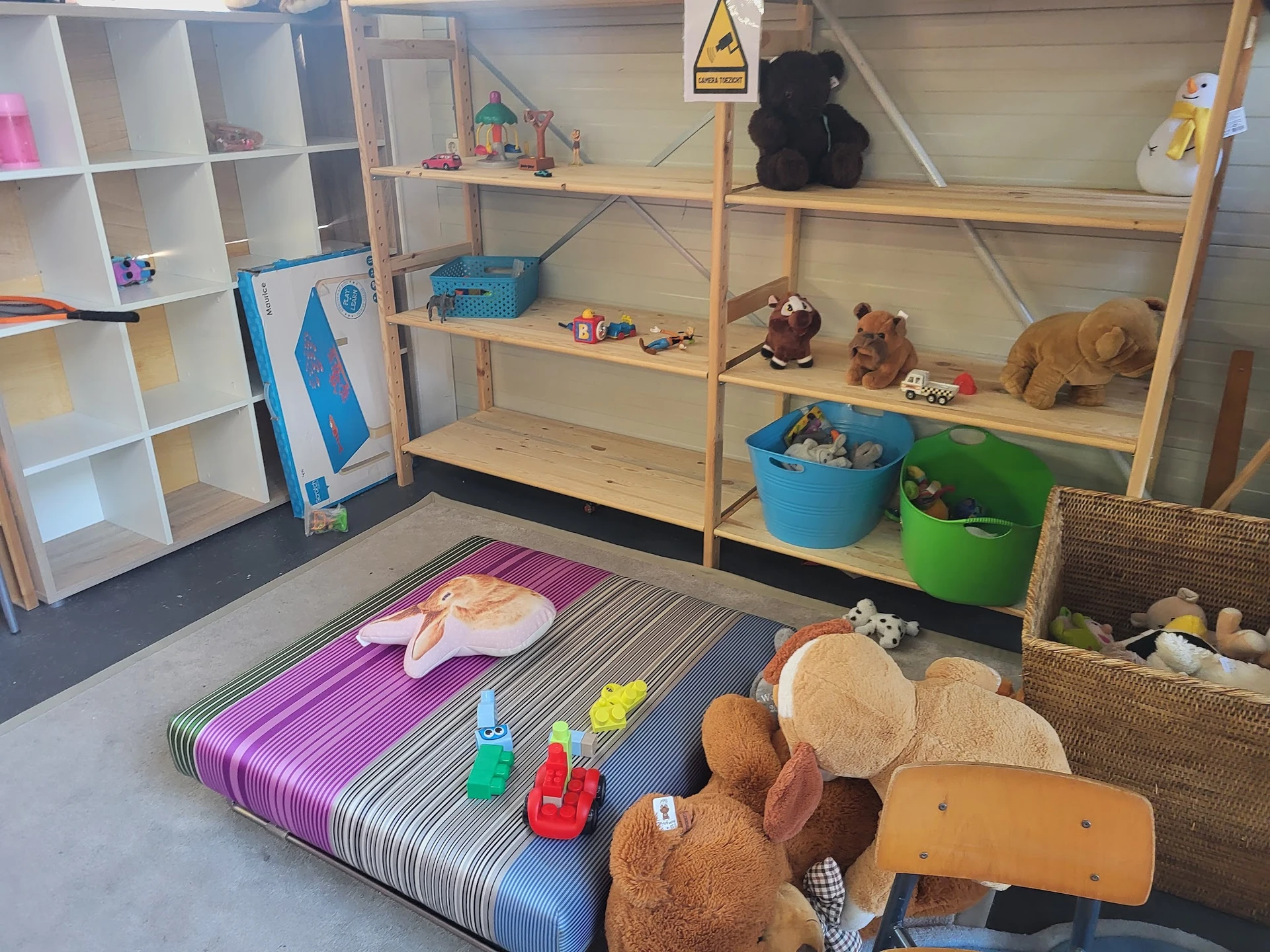 Kinderspeelhoek met speelmat, speelgoed, knuffels en opbergboxen in een kringloopwinkel