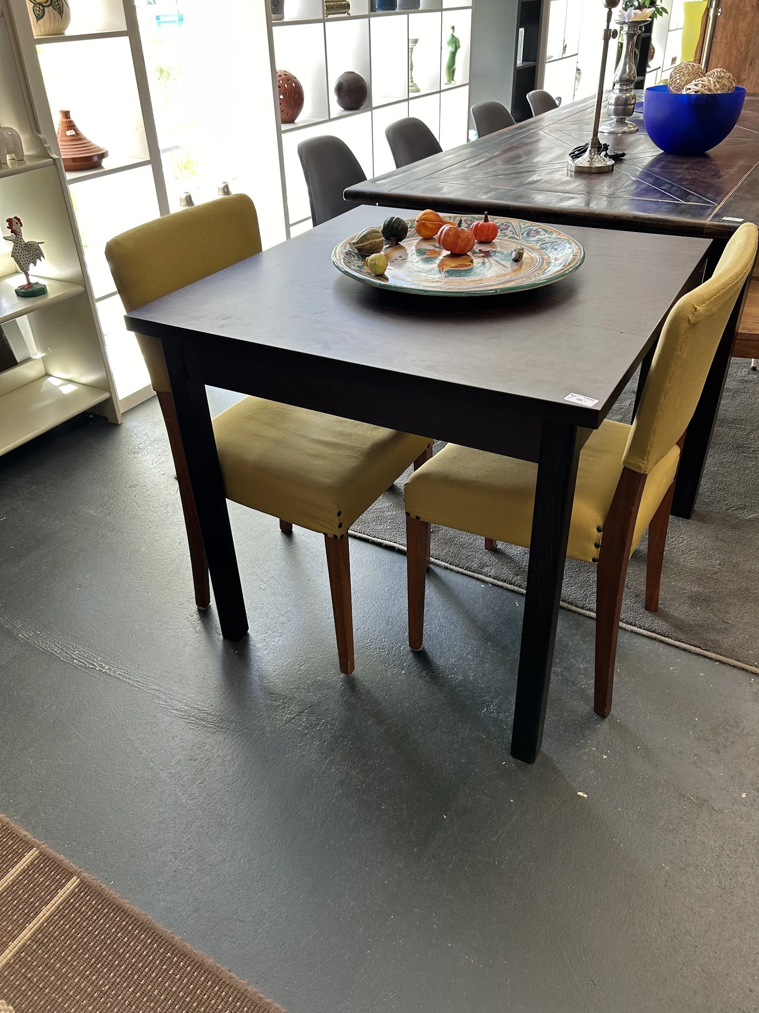 Zwarte eettafel met grijs blad en twee gele stoelen, daarop een decoratief bord met voedsel