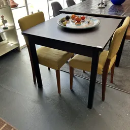 Zwarte eettafel met grijs blad en twee gele stoelen, daarop een decoratief bord met voedsel