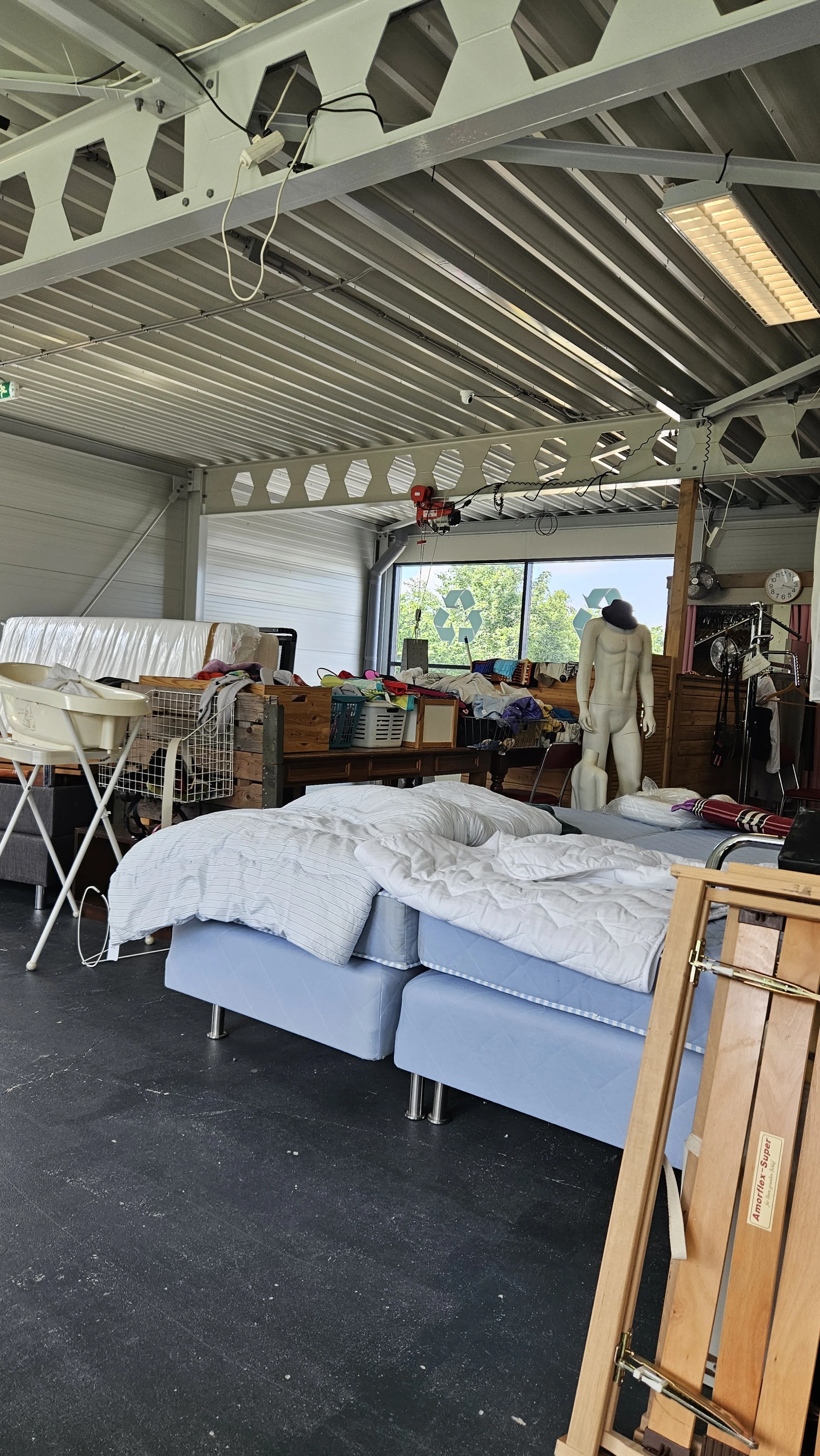 Binnenaanzicht van kringloopwinkel met bed, kleding, meubels en diverse spullen
