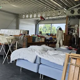 Binnenaanzicht van kringloopwinkel met bed, kleding, meubels en diverse spullen