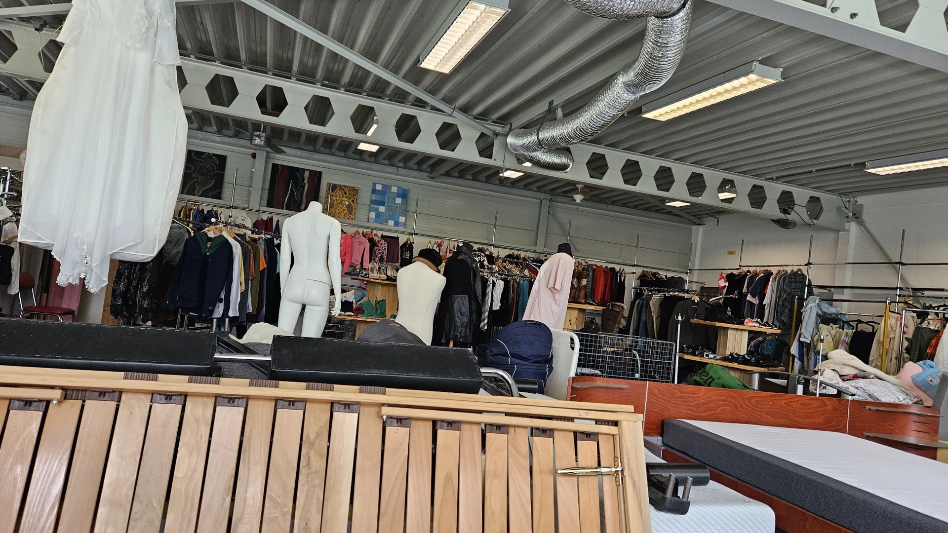 Interieur van kringloopwinkel met kledingrekken, mannequins en uitgestalde kleding onder fluorescente verlichting