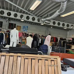 Interieur van kringloopwinkel met kledingrekken, mannequins en uitgestalde kleding onder fluorescente verlichting