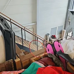 Diverse gebruikte spullen op een trap: tennisracket, roze sportschoenen, kleding en ander huishoudelijk goed