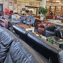 Diverse tweedehands meubels uitgestald in de winkel, waaronder leren banken en stoelen in verschillende kleuren