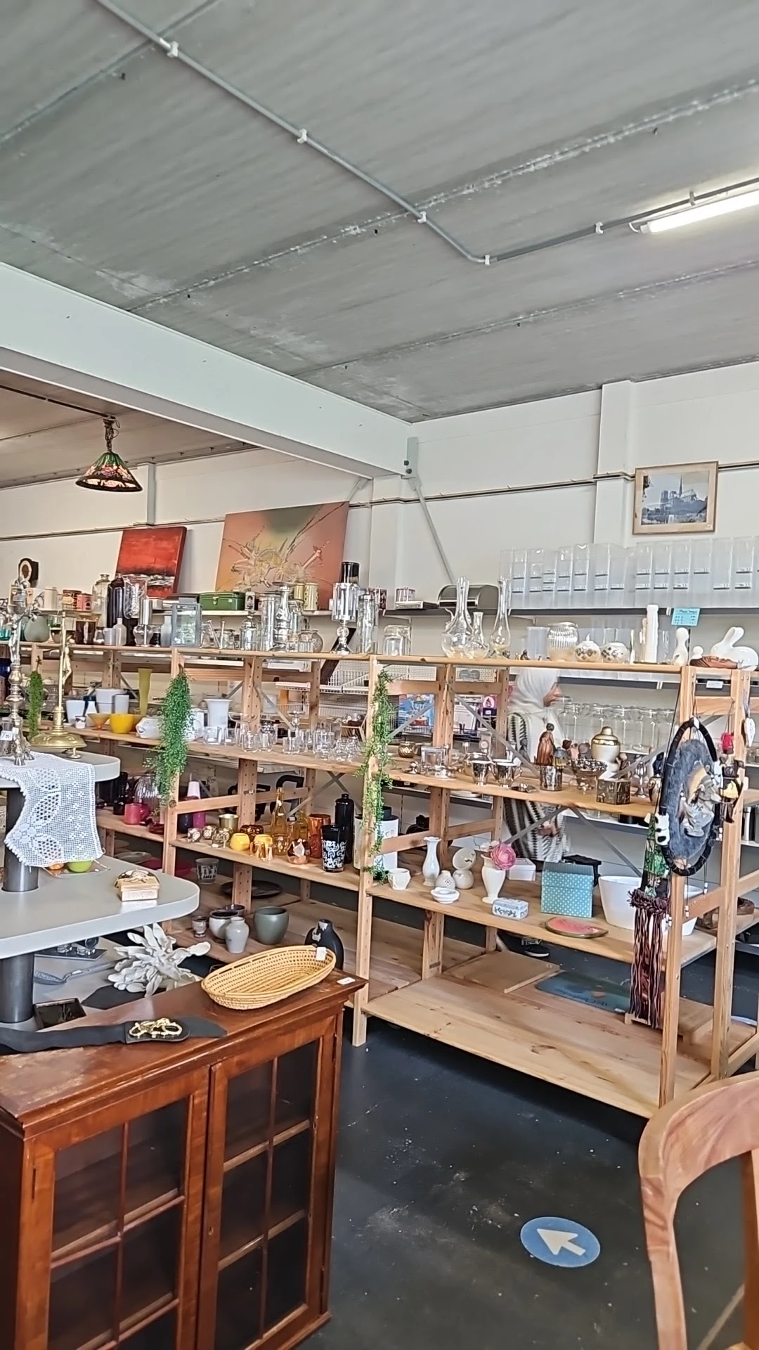 Houten stellingen vol met diverse tweedehands huishoudspullen, servies, decoratie en andere items in een kringloopwinkel