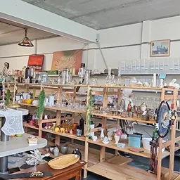 Houten stellingen vol met diverse tweedehands huishoudspullen, servies, decoratie en andere items in een kringloopwinkel