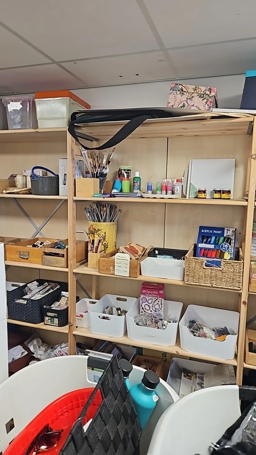 Houten stellingkast met kunstbenodigdheden: kwasten, verftubes, acrylverf, schetsblokken en andere creatieve materialen netje