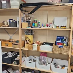Houten stellingkast met kunstbenodigdheden: kwasten, verftubes, acrylverf, schetsblokken en andere creatieve materialen netje