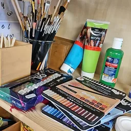 Verzameling kunstbenodigdheden: verfkwasten, acrylverf, olieverf, verfpaletten en tekensetjes op een tafel