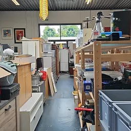 Winkelvloer van kringloopwinkel met houten stellingen, dozen en diverse tweedehands spullen