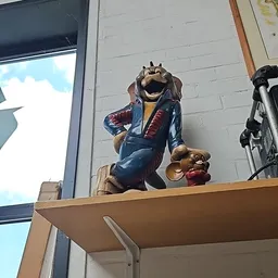 Groot houten beeldhouwwerk van een lachend dier in kleding op een houten balk buiten de winkel