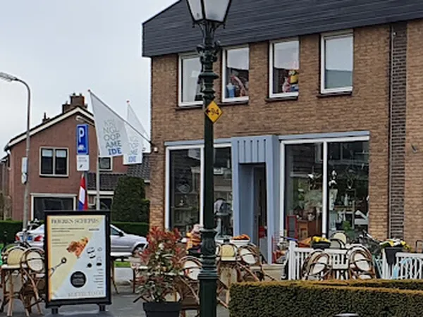Voorgevel van kringloopwinkel met bruine bakstenen muur, grote ramen, witte deuren en etalages met spullen, terras met stoele