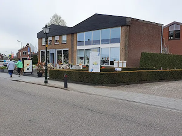 Voorgevel van moderne kringloopwinkel met grote ramen, bakstenen gevel en groene heg