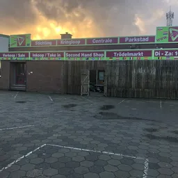 Gevel van kringloopwinkel met groene letters en verschillende afdeling-aanduiding tegen zonsondergang