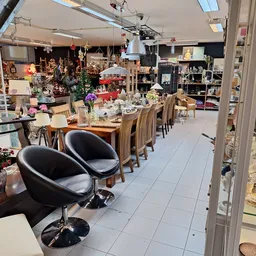 Ruim interieur van kringloopwinkel met eettafel, stoelen, diverse meubels en decoratieartikelen langs de wanden