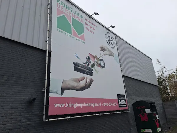Gevel van kringloopwinkel met groot reclamebord en ingang met rode deur