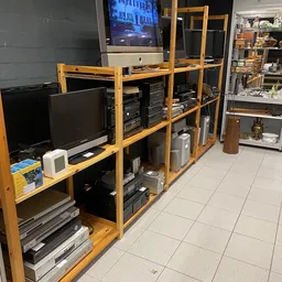 Houten stellingen met elektronische apparatuur zoals monitoren, computers en printers in een kringloopwinkel