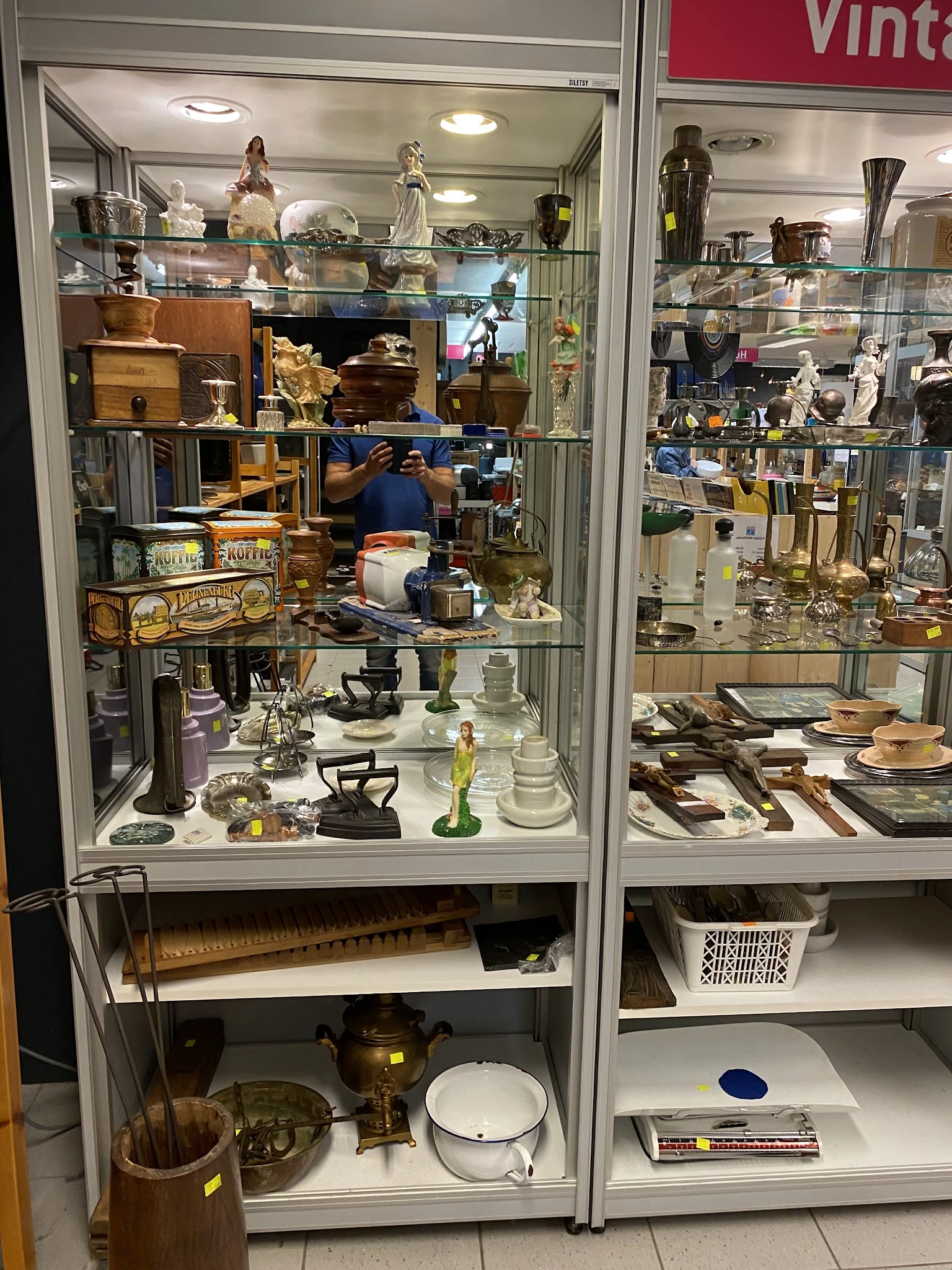 Glazen vitrinekasten met uitgestalde tweedehands huishoudspullen, servies, beeldjes en decoratieve items
