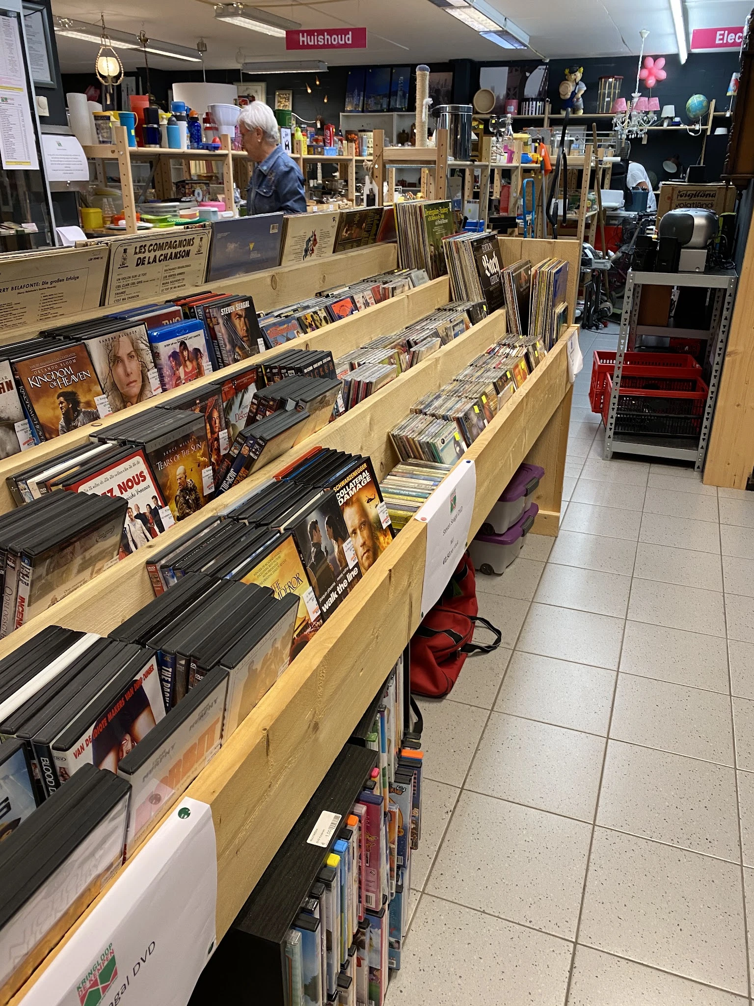 Houten stellingen met dvd's, blu-rays en cd's uitgestald in een kringloopwinkel