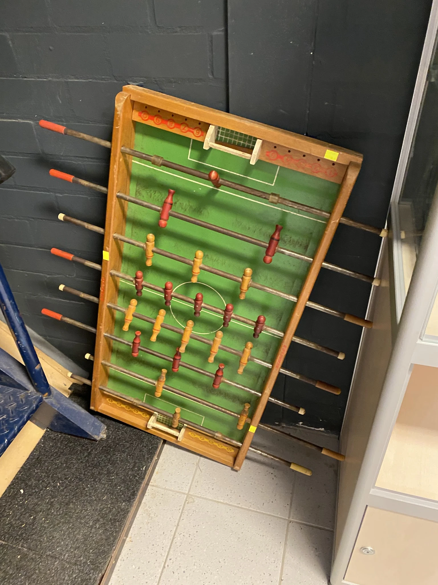 Tafelvoetbalspel met houten frame en groene speelveld met rode en gele spelers