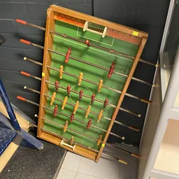 Tafelvoetbalspel met houten frame en groene speelveld met rode en gele spelers