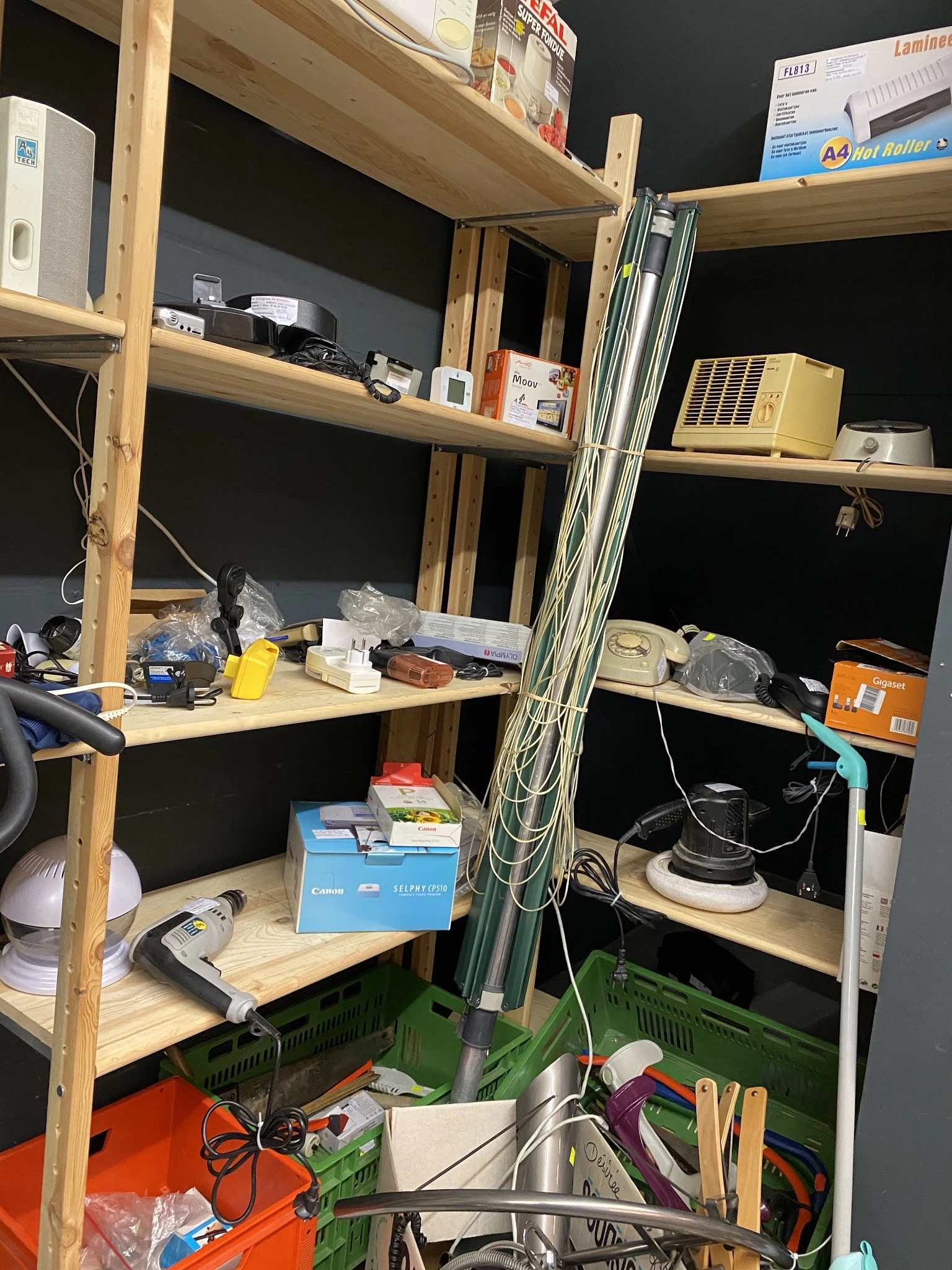 Houten stellingen met elektronische apparaten, kabels en diverse spullen in een kringloopwinkel
