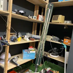 Houten stellingen met elektronische apparaten, kabels en diverse spullen in een kringloopwinkel