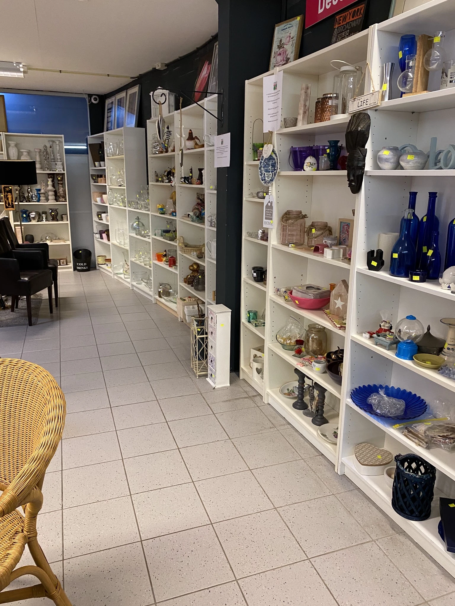 Witte stellingen vol serviesgoed, decoratieve items en blauwe flessen in een kringloopwinkel