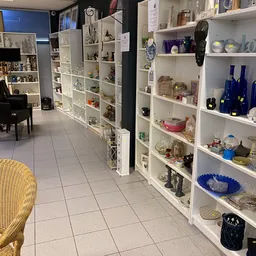 Witte stellingen vol serviesgoed, decoratieve items en blauwe flessen in een kringloopwinkel