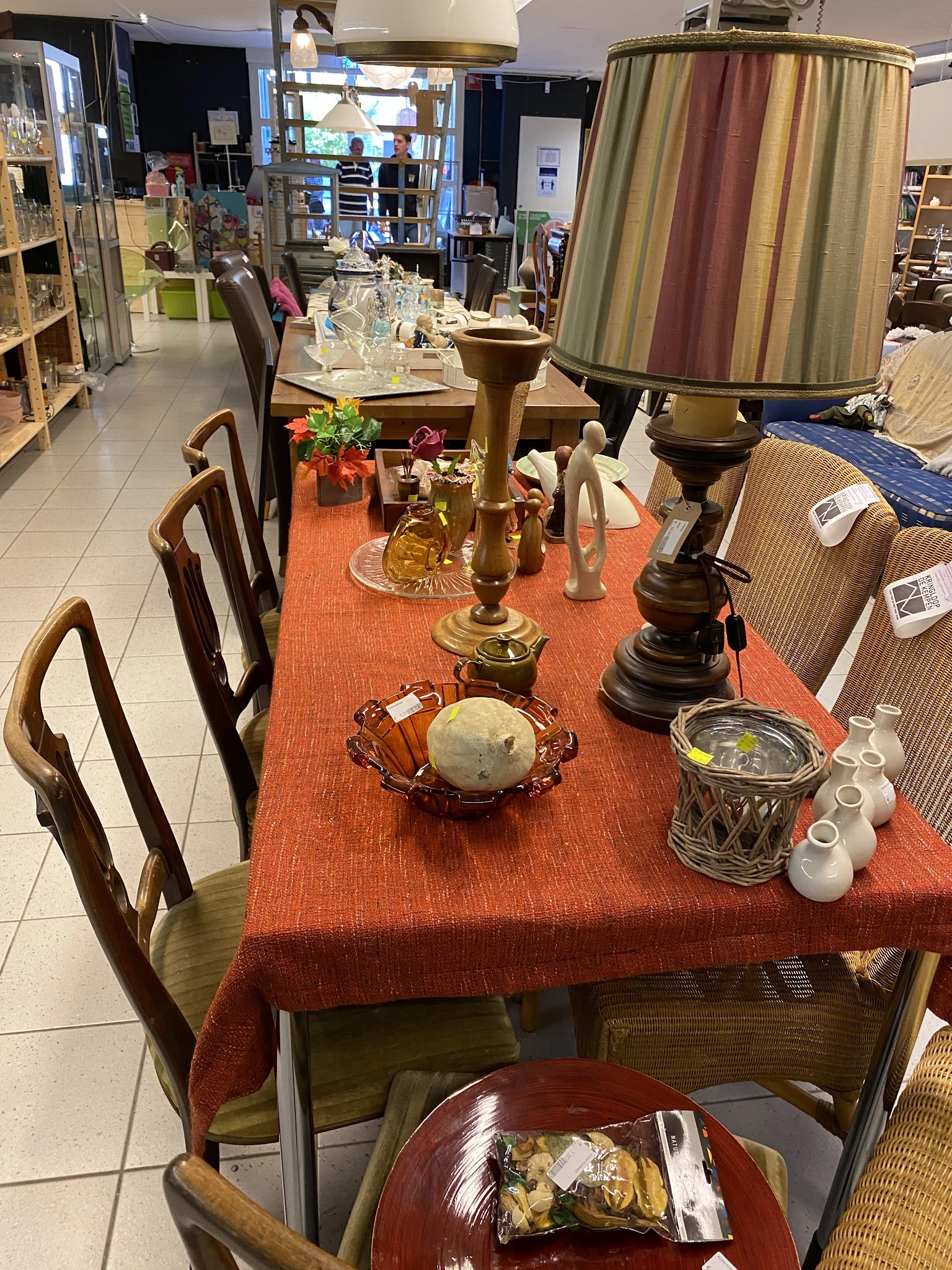 Tafel met oranje loper gedekt met diverse decoratieve voorwerpen: kandelaars, bloemen, beeldjes en aardewerk
