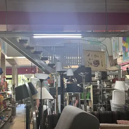 Binnenaanzicht van kringloopwinkel met lampen, stoelen en huishoudelijke spullen op stellingen