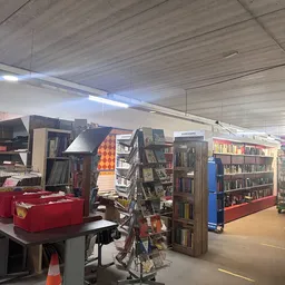 Winkelvloer met boeken en media in stellingen, rode tafel met spullen, heldere zaalsverlichting