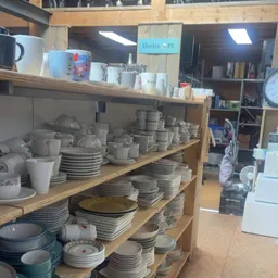 Houten stellingen vol met gestapeld servies, borden en kopjes in grijze en witte tinten